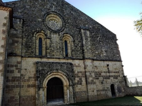 Façade romane de l’abbatiale de Flaran. Cette façade occidentale (XIIe – XIIIe siècles) est soulignée par deux contreforts. Le porche, sans tympan, qui repose sur les colonnes de piédroits, s’ouvre par une triple voussure. Deux ouvertures en plein cintre, surmontées d’une rose (“oculus”), laissent pénétrer la lumière du couchant, dans la nef. Bâtie en pierre de taille vers 1180, l’église Notre Dame de Flaran est remarquable par ses proportions, par la rigueur de son plan cistercien et par son état de conservation, malgré des dimensions modestes (40 m de long par 19 m de large). Elle demeure caractéristique de l’art roman méridional de la deuxième moitié du XIIe siècle. Photo © François Collombet